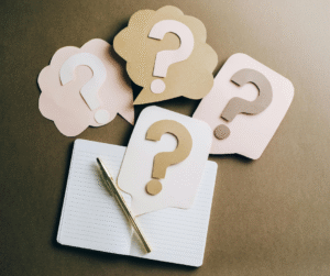 An open journal, pen, and several pieces of paper cut in the shape of question marks.