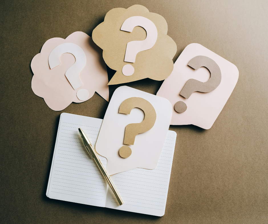 An open journal, pen, and several pieces of paper cut in the shape of question marks.