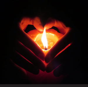 hands cup a candle, forming the shape of a heart